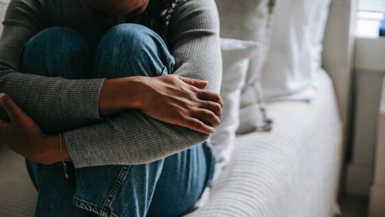 crop pitiful black woman embracing knees on bed